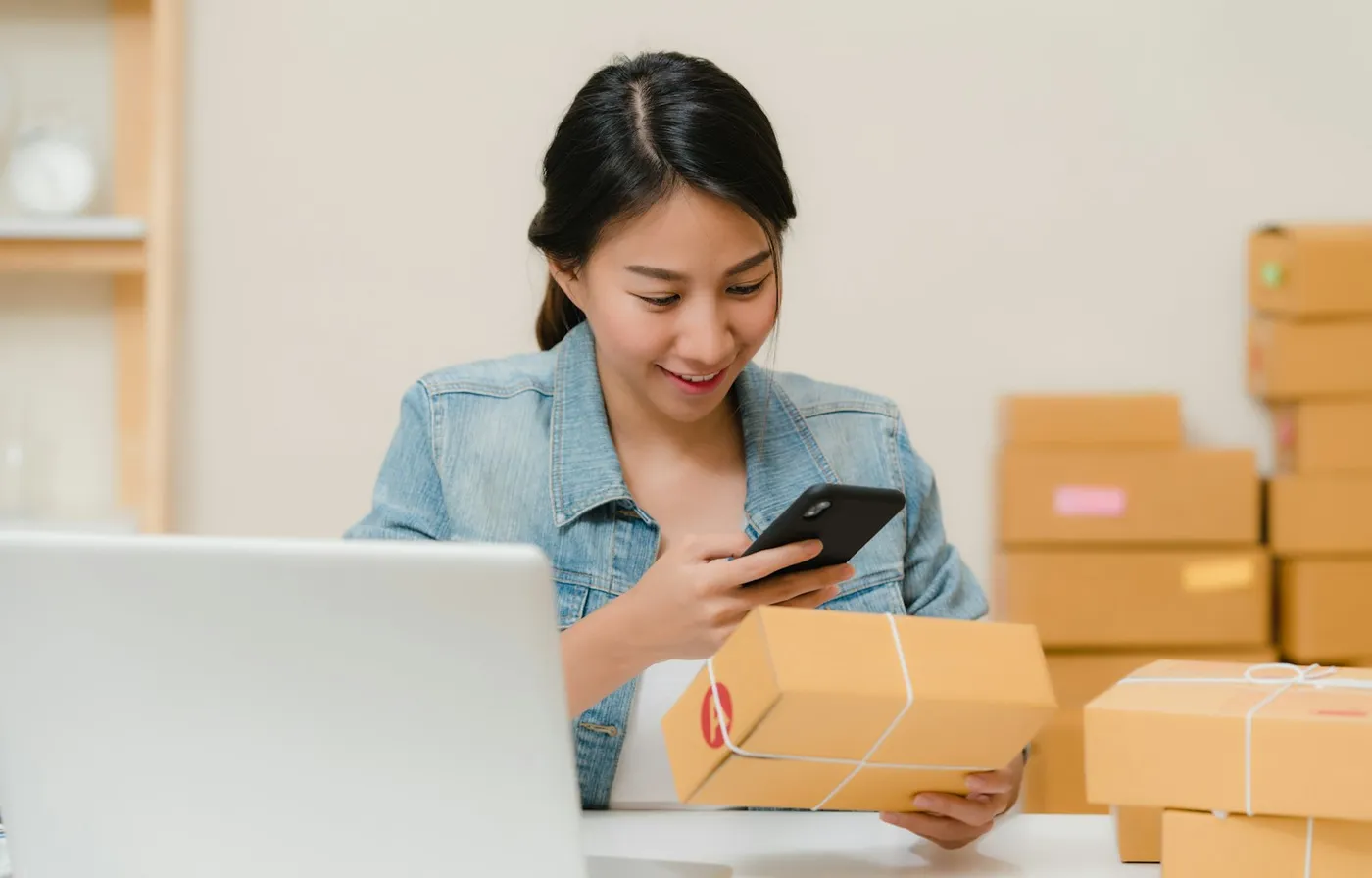 Online store owner checking a parcel next to a laptop and stacked shipping boxes