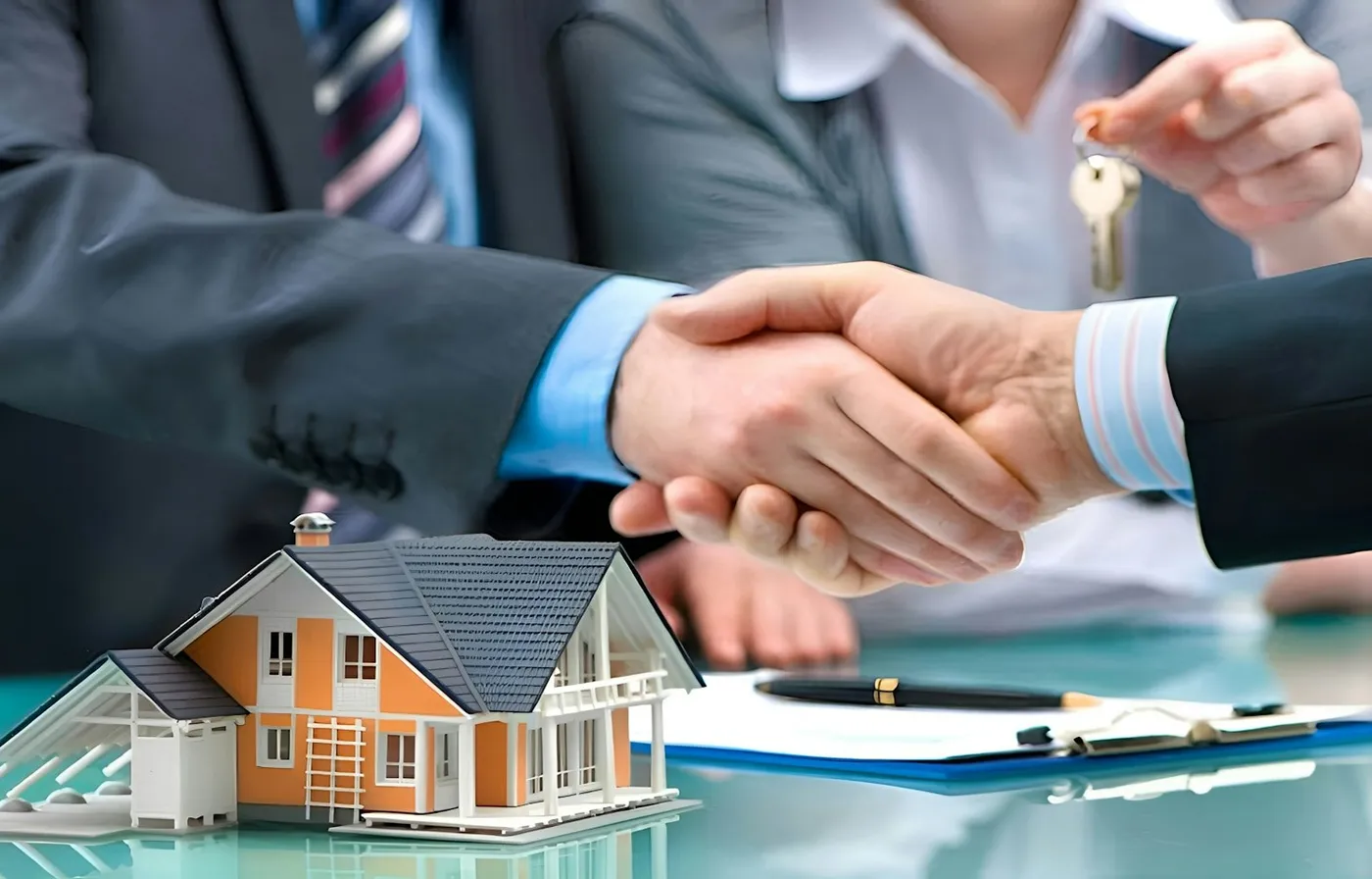 Real estate agent handing over house keys with a handshake beside a model home